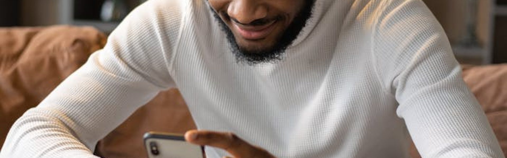 Positive black man using smartphone while sitting on sofa